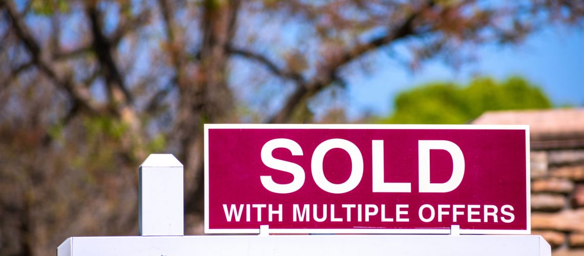 SOLD With Multiple Offers real estate sign near purchased house indicates hot seller's market in the desired neighborhood. Blurred outdoor background.